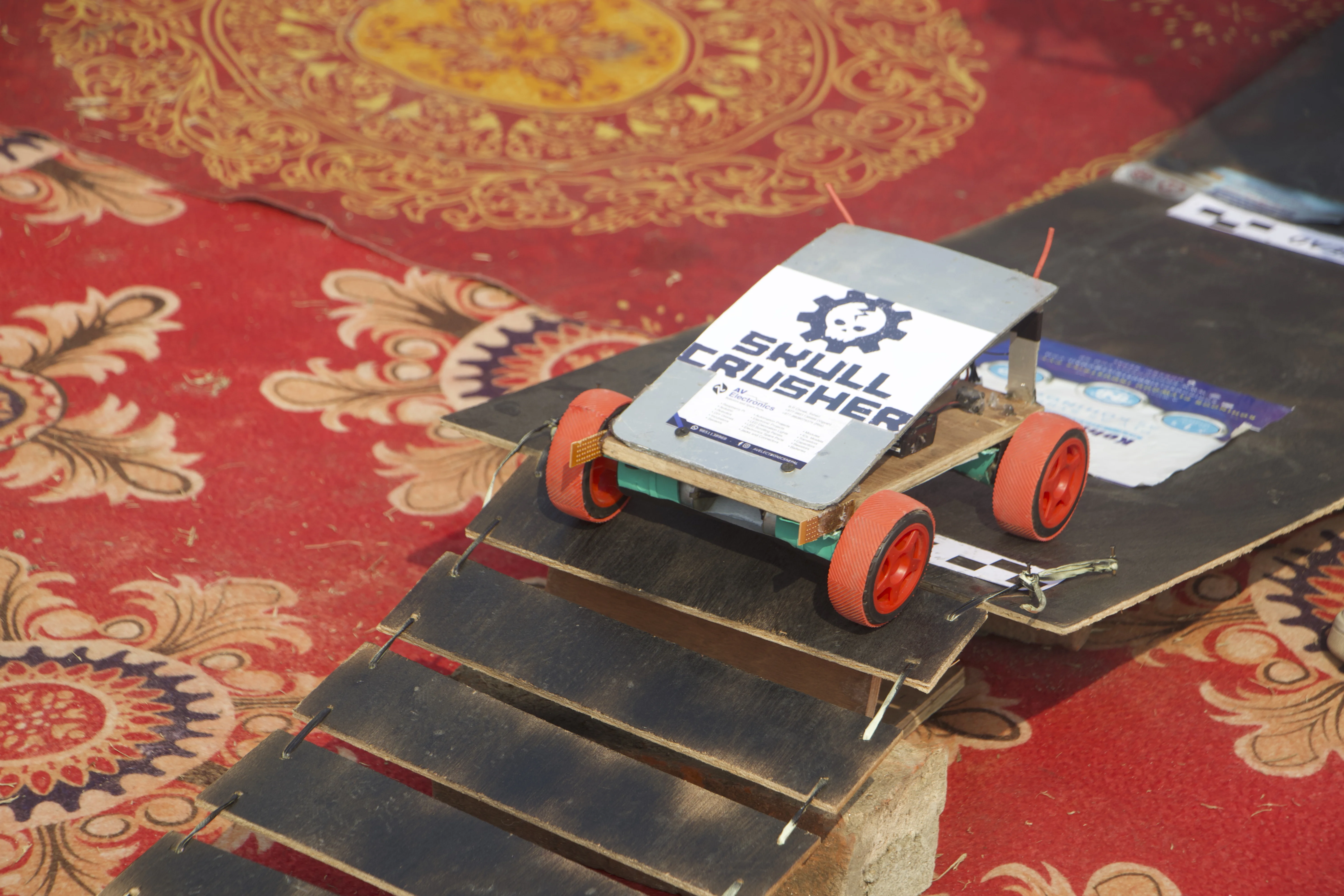 Small wheeled robot car displayed on a ramp during a Koshi Mini Yantra event activity.